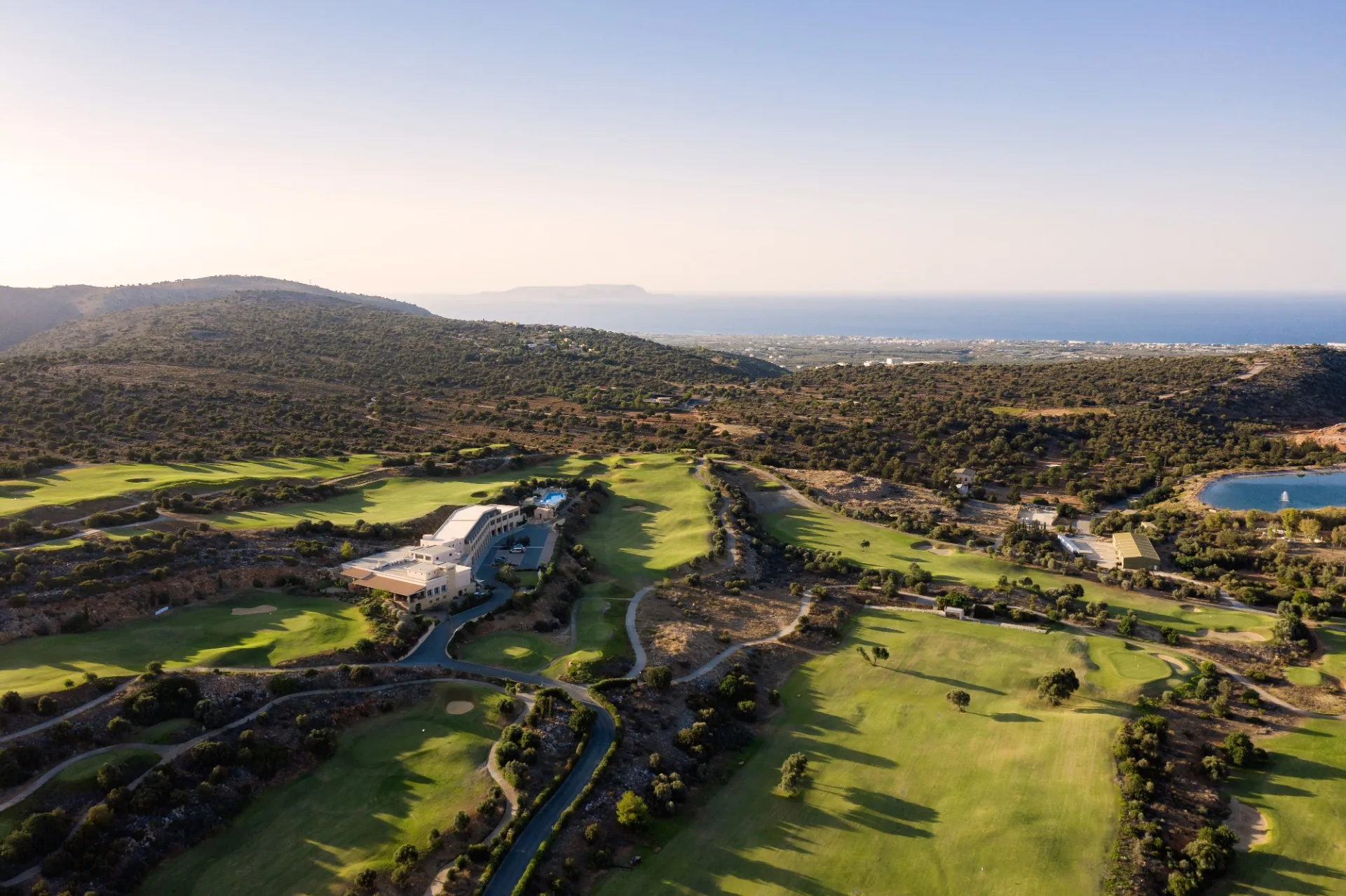 Luftaufnahme des Crete Golf Club Hotels zwischen den Fairways, im Hintergrund das Meer