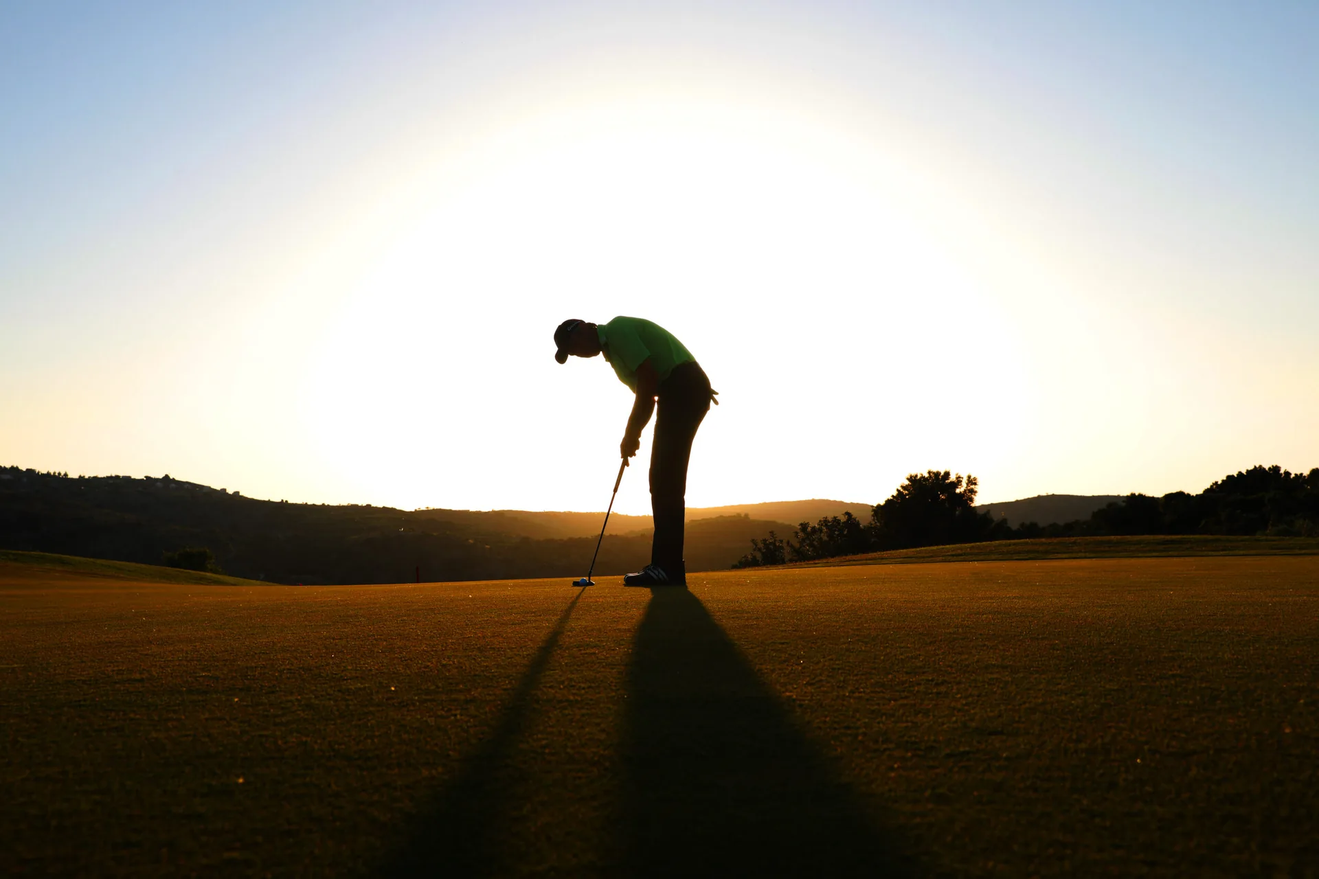 Golfer beim Putten im Gegenlicht der tiefstehenden Sonne
